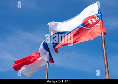 Die slowakische Flagge und die tschechische Flagge, die im Wind auf hölzernen Fahnenmasten gegen den blauen Himmel weht Stockfoto