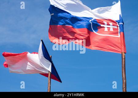 Die slowakische Flagge und die tschechische Flagge, die im Wind auf hölzernen Fahnenmasten gegen den blauen Himmel weht Stockfoto