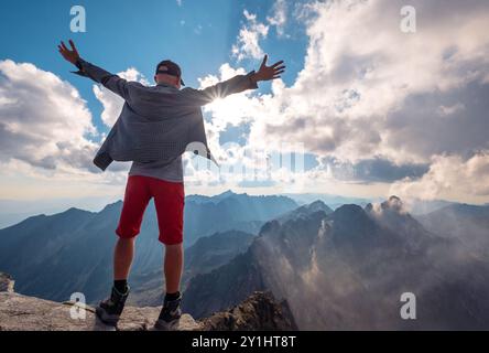 Trekker mit erhobenen Armen auf dem Rysy-Gipfel, 2499 m hoch, die hohe Tatra-Bergkette bedeckt neblige Wolken am frühen Morgen mit unglaublichem Licht A Stockfoto