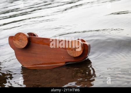 Ein hölzerner Spielzeugwagen kippte in einem See um und überflutet mit Wasser. Wird für Kfz-Versicherungen oder für Wasserschäden an Fahrzeugen verwendet. Stockfoto