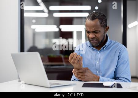 Büroangestellte fühlen sich bei der Benutzung des Laptops Schmerzen am Handgelenk, was ein Unbehagen durch sich wiederholende Strain-Verletzungen zum Ausdruck bringt. Mann, der am Schreibtisch sitzt und Linderung von Schmerzen und Unannehmlichkeiten während der Arbeit sucht. Stockfoto