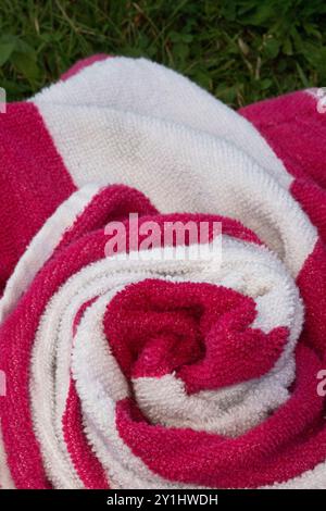 Nahaufnahme, weiß-rosa gestreiftes Handtuch spiralförmig auf dem Gras, hoher Kontrast, schwere Textur, Hintergrund, abstrakt, Material, Textil, Stoff mit Kopie Stockfoto