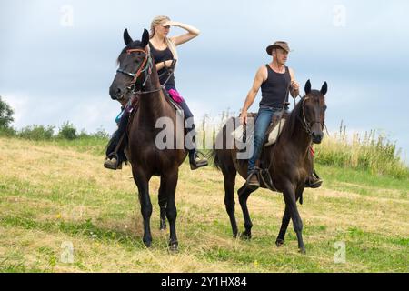 Zwei Personen reiten durch ein grasbewachsenes Feld, einer blickt in die Ferne, während der andere die Zügel hält Stockfoto