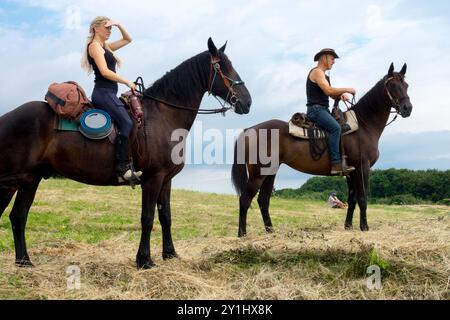 Zwei Reiter auf einem grasbewachsenen Feld, eine Frau, die in die Ferne blickt, und ein Mann, der auf seinem Pferd sitzt und einen Hut trägt Stockfoto