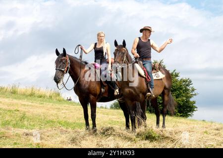 Ein Mann und eine Frau reiten Pferde auf einem grasbewachsenen Feld unter bewölktem Himmel an einem sonnigen Tag Stockfoto