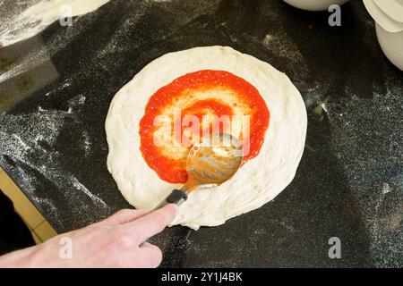 Ansicht von oben nach unten: Tomatensauce auf Pizzateig mit einem Löffel Stockfoto