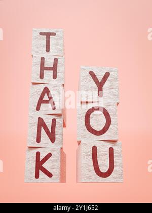 Weiß bemalte Holzwürfel mit roten Buchstaben, die in Thank You-Worten auf rosa Hintergrund angeordnet sind Stockfoto