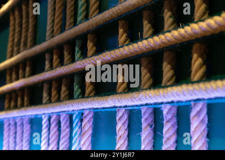 Gekreuzte Seile hängen als abstrakte Dekoration an der Wand. Hausgemachte originelle Inneneinrichtung mit grünem Hintergrund und farbigen LED-Leuchten, der Ro Stockfoto