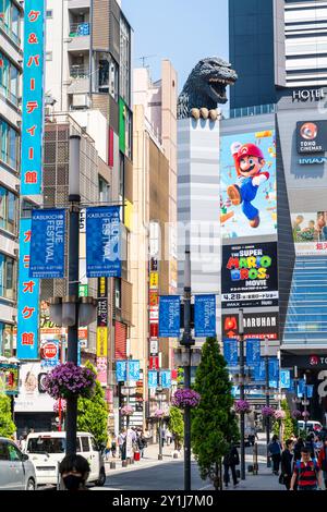 Blick auf die Central Road in Shinjuku, dem Unterhaltungsviertel, mit dem berühmten Godzilla Head, der über die Spitze des Toho Kinogebäudes blickt. Blauer Himmel. Stockfoto