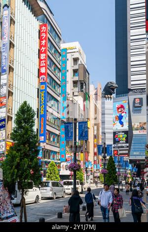 Blick auf die Central Road in Shinjuku, dem Unterhaltungsviertel, mit dem berühmten Godzilla Head, der über die Spitze des Toho Kinogebäudes blickt. Blauer Himmel. Stockfoto