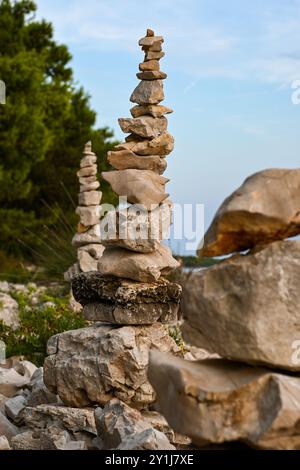 Stone cairns balancieren an einem felsigen Strandufer mit Kiefern im Hintergrund. Stockfoto