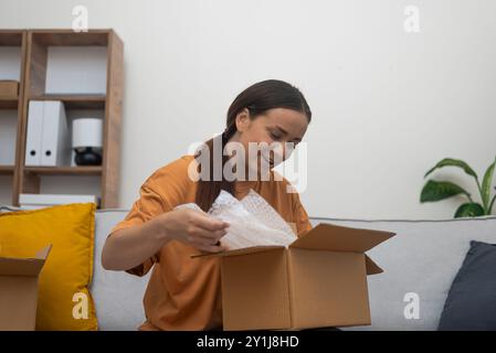Bequem sitzend erkundet eine Frau ihre Lieferung und drückt ihre Freude nach einem Online-Kauf aus. Stockfoto