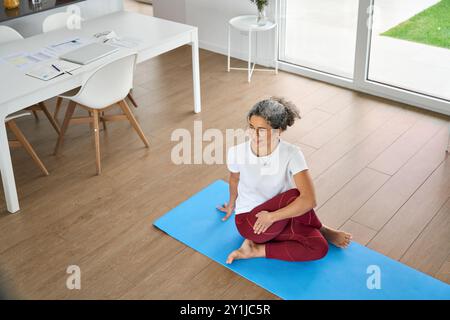 Glückliche, gesunde Frau mittleren Alters, die Yoga-Übungen macht, zu Hause sitzend. Stockfoto