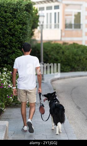 Ein Mann geht mit seinem Hund auf einem Bürgersteig. Der Hund ist schwarz und weiß und trägt eine Leine. Die Szene ist friedlich und ruhig, mit dem Mann Stockfoto