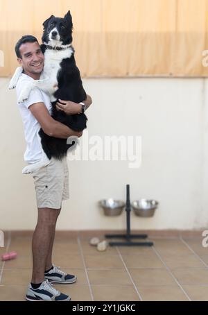 Ein Mann hält einen großen schwarz-weißen Hund. Der Hund trägt ein Halsband Stockfoto