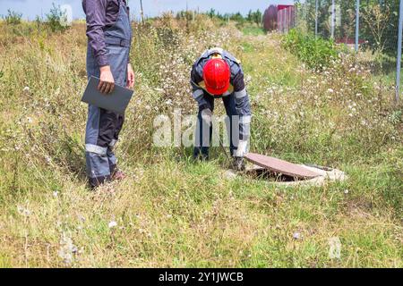 Klempner arbeiten in der Nähe eines offenen Brunnens. Die Männer öffneten die Mannlochabdeckung, um die Rohre zu reparieren. Stockfoto