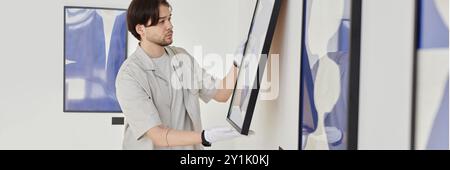 Kopfbild eines jungen Mannes, der abstrakte Kunstbilder an die Wand hängte, während er einen Ausstellungsraum für moderne Kunstgalerien plante Stockfoto