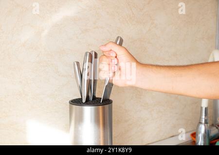 Männliche Hand, die Küchenmesser vom Stand in der Küche in der Wohnung abhebt Stockfoto