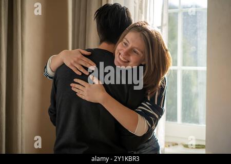 Glückliches junges Mädchen umarmt ihren Freund, freut sich über das Treffen, steht neben dem Fenster, lächelndes Gesicht in Nahaufnahme, Frau beginnt eine romantische Beziehung Stockfoto