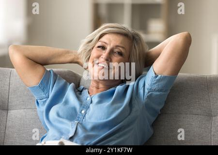 Entspannte, reife Frau, die auf dem Sofa liegend in die Kamera schaut Stockfoto