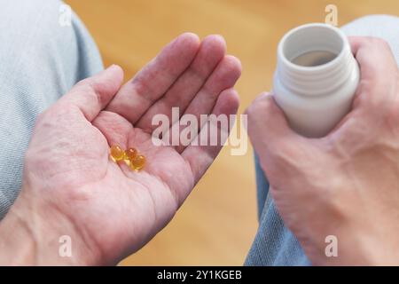 Ein Mann goss Vitamin D3 Kapseln aus einer Plastikflasche in seine Handfläche. Stockfoto