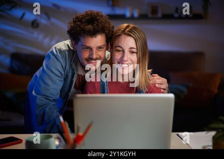 Zwei glückliche junge Kaukasier zusammen, die nachts auf den Schreibtisch im Wohnzimmer schauen. Stockfoto