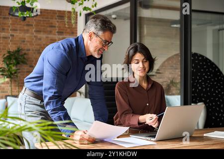 Zwei glückliche, beschäftigte Führungskräfte, die im Büro mit einem Laptop arbeiten. Stockfoto
