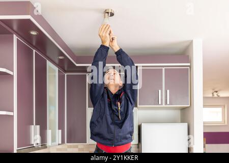 Man schraubt Glühbirne in den Kronleuchter ein. Reifer Mann, der ein energiesparendes Deckenlicht in einer Küche wechselt Stockfoto