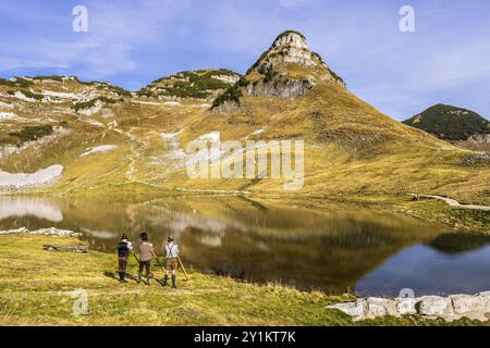 Drei Männer spielen das Alphorn am Augstsee am Mount Loser. Das österreichische Alphorntrio Klangholz. Der Atterkogel im Hintergrund. Herbst, gutes Wetter Stockfoto