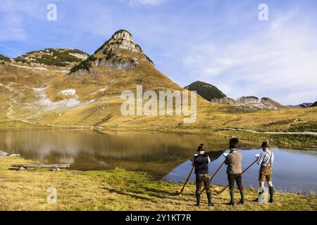 Drei Männer spielen das Alphorn am Augstsee am Mount Loser. Das österreichische Alphorntrio Klangholz. Der Atterkogel im Hintergrund. Herbst, gutes Wetter Stockfoto