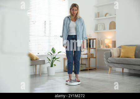 Wechseljahre, Gewichtszunahme. Besorgte Frau, die zu Hause auf der Waage steht Stockfoto