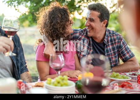 Paare mittleren Alters teilen sich intime Momente bei einer Dinner-Party im Freien. Romantische Picknickszene mit Wein und frischem Essen. Konzept von Liebe, Beziehungen, an Stockfoto