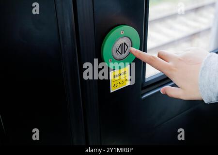 Eine Person drückt eine leuchtend grüne Taste an einer Tür, die wahrscheinlich als Eingangspunkt für ein Gebäude oder einen Raum dient Stockfoto