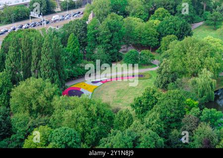 Blick aus der Vogelperspektive auf einen üppig grünen Park mit farbenfrohen Blumenbeeten in Mustern. Der Park ist von dichten Bäumen und einem gewundenen Pfad mit einem umgeben Stockfoto