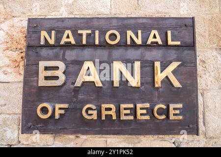 Rhodos-Stadt, Griechenland – 19. Juli 2024. Schild der griechischen Nationalbank mit goldenen Buchstaben auf einem Holzteller, an der Wand eines Gebäudes in Rhodos, Griechenland. Fo Stockfoto