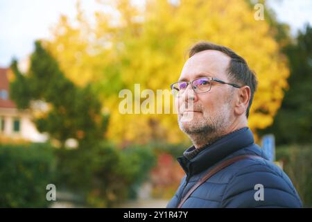 Herbstporträt eines gutaussehenden 50-jährigen Mannes, der draußen mit gelbem Laub posiert Stockfoto