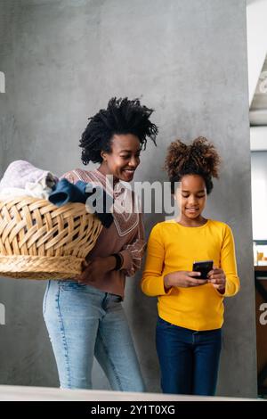 Glückliche alleinerziehende schwarze Mutter und Kind, die Hausarbeiten erledigen, Kind, das zu Hause Smartphone benutzt Stockfoto