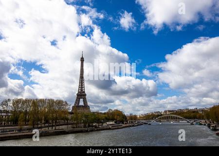 Unter einem leuchtend blauen Himmel steht der berühmte Eiffelturm hoch neben der seine, umgeben von üppigen Bäumen und sanften Wolken, und fängt den Charme der seine ein Stockfoto