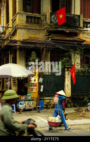 Urbane Vibes aus Hanoi mit Militärs auf dem Roller und Straßenverkäufern unter ihrem Hut. Stockfoto