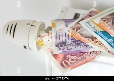 Britische Pfund liegen auf einem nicht verschraubten Heizkörper, Konzept, Finanzbudget. Heizkosten im Winter im Vereinigten Königreich Stockfoto