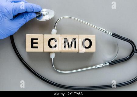 Wort ecmo auf Holzwürfeln geschrieben. Gesundheitskonzept für Krankenhaus, Klinik und Medizinwirtschaft. Stethoskop in der Hand des Arztes. Wunderschöner grauer Background Stockfoto