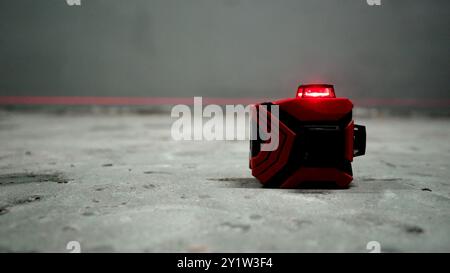 Laserkonstruktion mit roten Strahlen an der Wand. Renovierungs- und Bauarbeiten der Apartments. Installation einer Laserwaage für die Bodenreparatur. Stockfoto