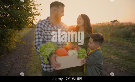 Die kaukasische Familie hält frisches Gemüse in der Box. Glückliche Frau Mutter weiblich kleiner Junge Kind Sohn Mann Vater männlich genießen Vitamin gesunde Lebensmittel Bauernhof Ernte Stockfoto