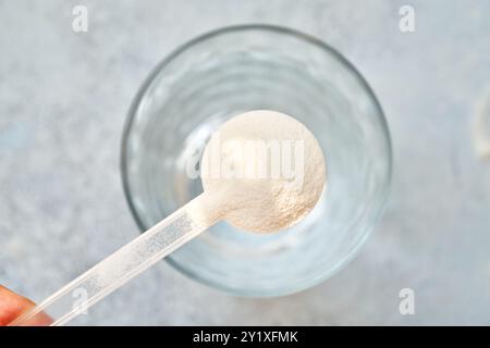 Kollagenpulver in einem Kunststoff-Messlöffel über einem Glas Wasser, Draufsicht Stockfoto