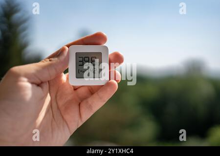 Ein kleines Thermometer wird in der menschlichen Hand gehalten und zeigt sehr hohe Sommertemperaturen an. Die Szene zeigt die Auswirkungen der globalen Erwärmung und tropischen Stockfoto