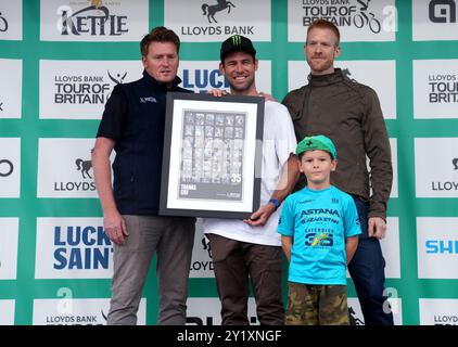 Mark Cavendish (Mitte) wird mit einer Fotocollage seiner rekordverdächtigen 35 Siege bei der Tour de France präsentiert - präsentiert von Ed Clancy OBE (links) nach der sechsten Etappe der Lloyds Bank Tour of Britain 2024 von Lowestoft nach Felixstowe. Bilddatum: Sonntag, 8. September 2024. Stockfoto