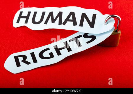 Ein detailliertes Vorhängeschloss enthält zwei Papierstücke mit der Aufschrift „Menschenrechte“, die in der Mitte des Bildes mit einem kräftigen roten Hintergrund platziert sind Stockfoto