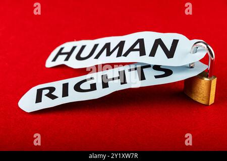 Ein Metallschloss hält zwei Papiere zusammen mit den Worten "Menschenrechte" in fetten Buchstaben, zentriert auf einem kräftigen roten Hintergrund Stockfoto