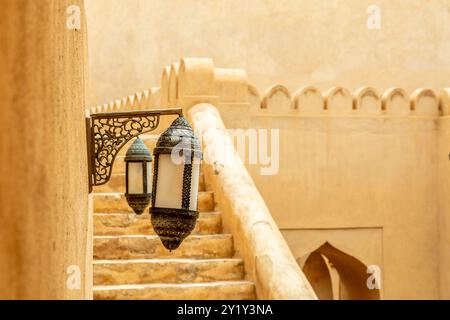 Traditionell dekorierte Wandlampen im Innenhof der Festung der arabischen Zitadelle mit Treppen und Wänden im Hintergrund, Nizwa, Sultanat Oman Stockfoto