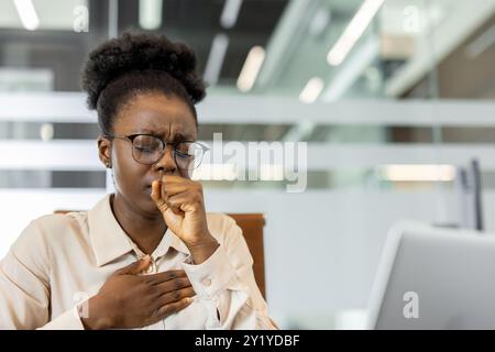 Afroamerikanische Geschäftsfrau, die im Büro unangenehm ist und Husten hat. Zeigt Stress, Krankheit oder Ermüdung am Arbeitsplatz an. Hebt die Herausforderungen hervor, denen sich Fachkräfte im Gesundheitsbereich gegenübersehen Stockfoto